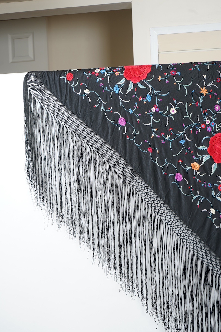 A late 19th century Chinese black silk polychrome floral embroidered shawl with long silk fringing. Embroidered with large red roses and an all over multi coloured floral sprig design. 123cm x 108cm. Condition, silk and